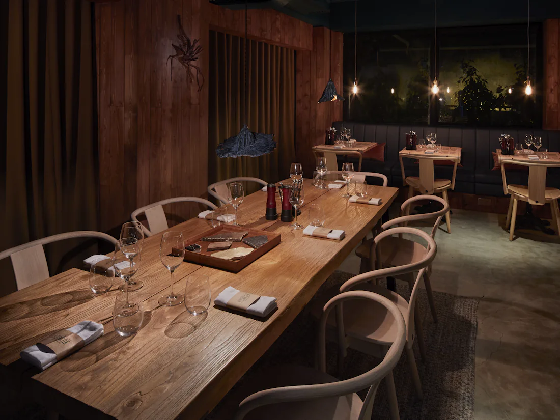 A long timber table laid for ten under low pendant lights, with the rest of the room behind it.