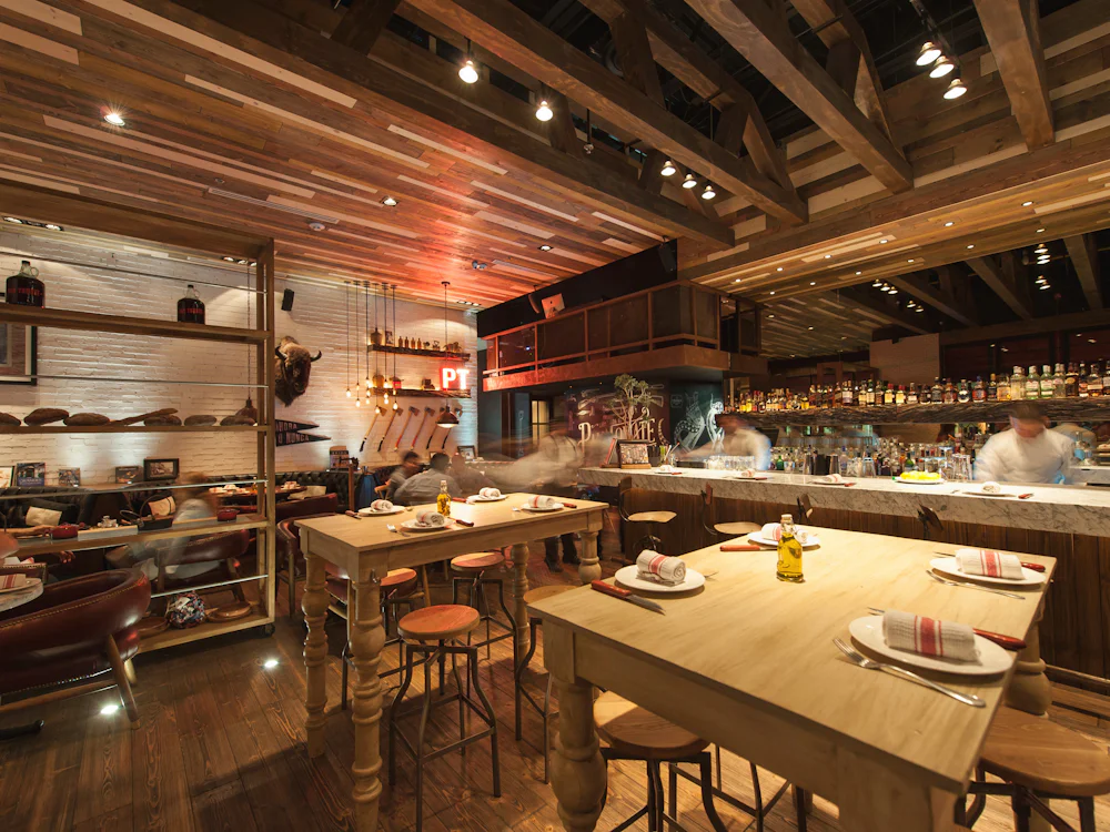 The room from the pass: timber beams, a communal table and stools drawn up to the kitchen.